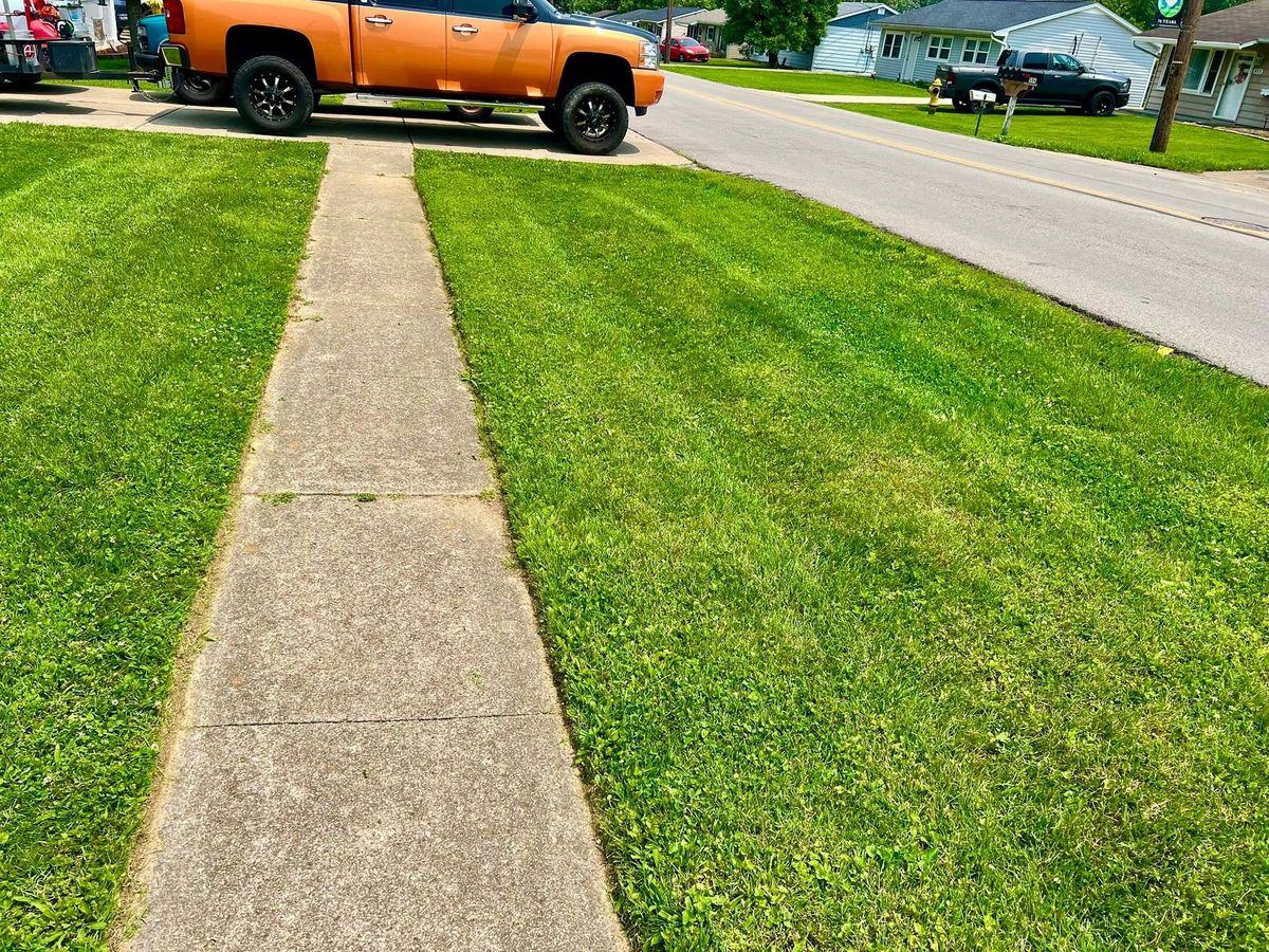 Sharp mowed edge running down both sides of a concrete sidewalk, the orange truck at the top of the frame